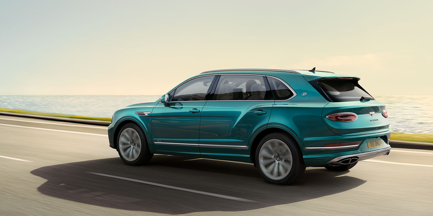 Bentley Monterrey Bentley Bentayga Extended Wheelbase Azure luxury SUV rear three quarter in Topaz Blue by Mulliner paint, driving on an ocean road.
