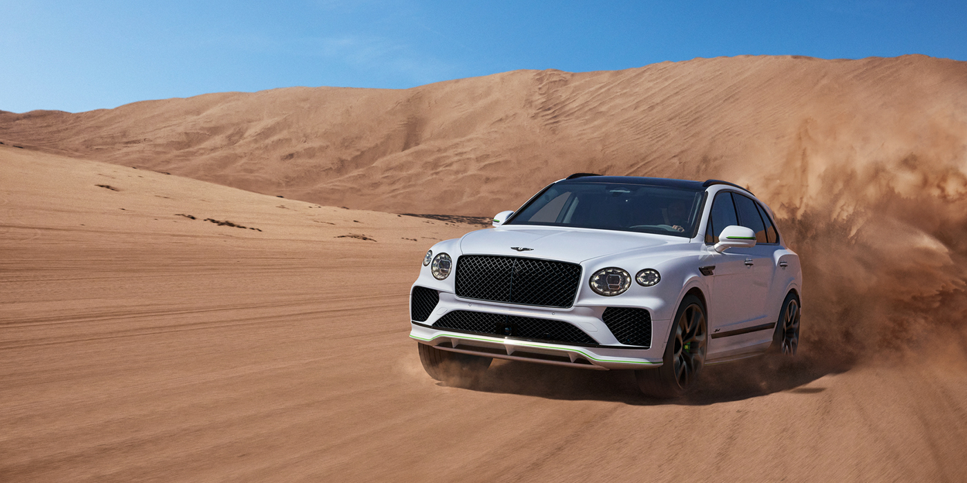 Bentley Monterrey Bentley Bentayga Speed SUV front three quarter in Snow Quarts Pearlescent by Mulliner white paint driving dynamically through the desert