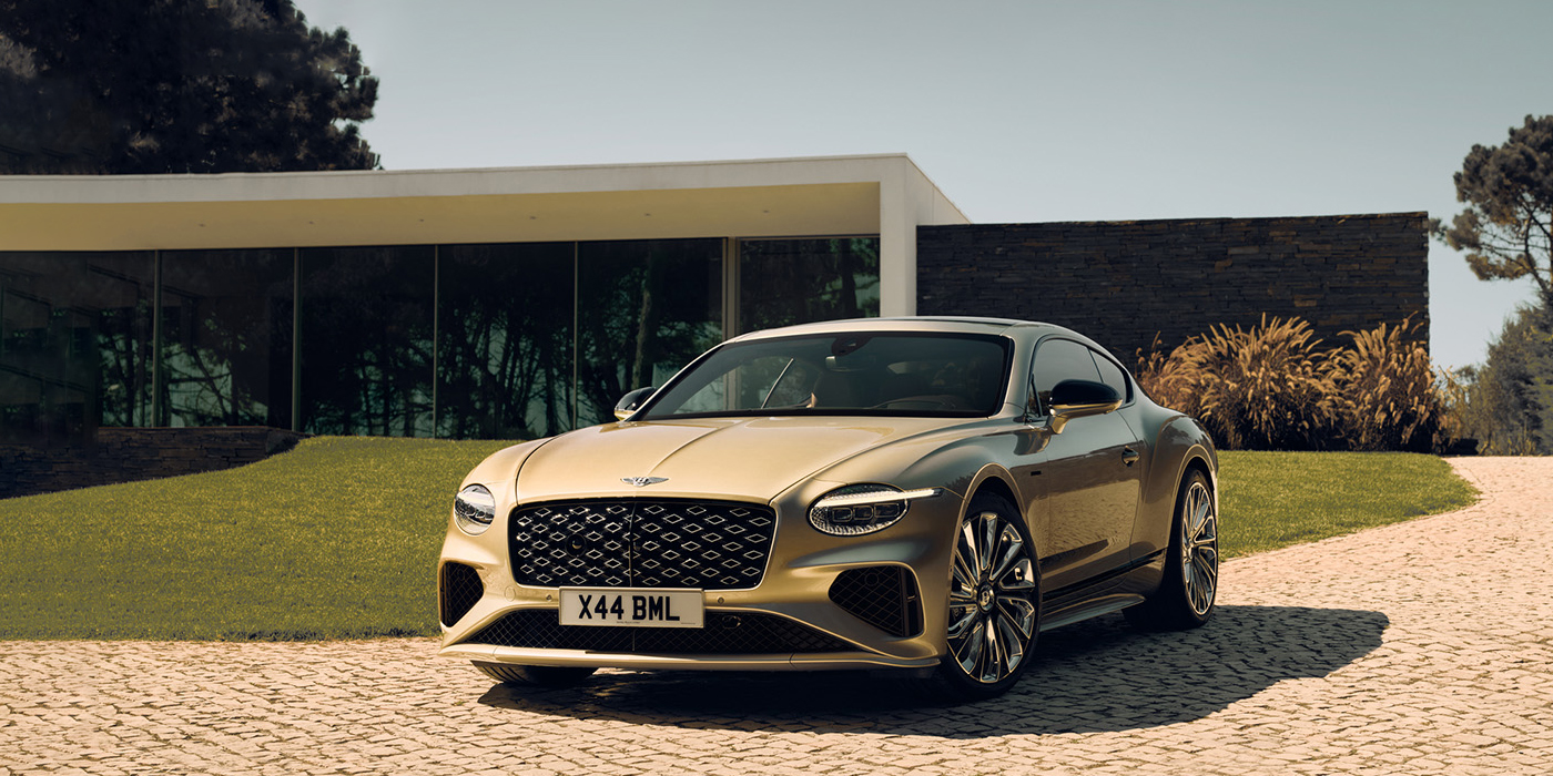 Bentley Monterrey Bentley Continental GT Mulliner coupe front three quarters in Patina paint parked outside a glass fronted building with a grass lawn behind it