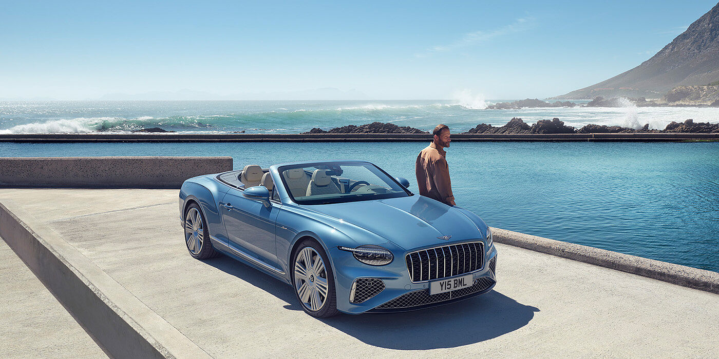 Bentley Monterrey New Bentley Continental GTC Azure convertible front view in Light Windsor blue paint with 22 inch ten spoke wheels parked by the sea in the sunshine