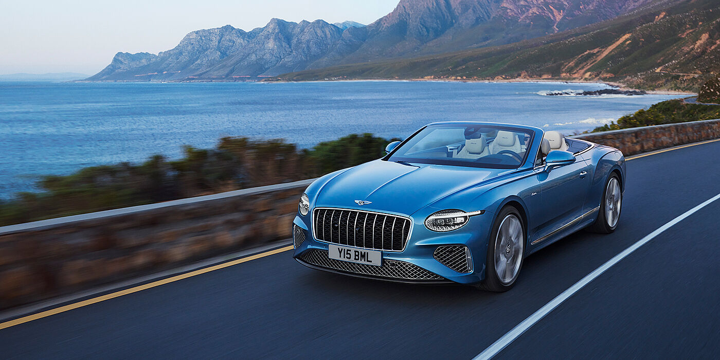 Bentley Monterrey New Bentley Continental GTC Azure convertible in Light Windsor blue paint with 22 inch Azure wheels and chrome grill, driving dynamically by the sea