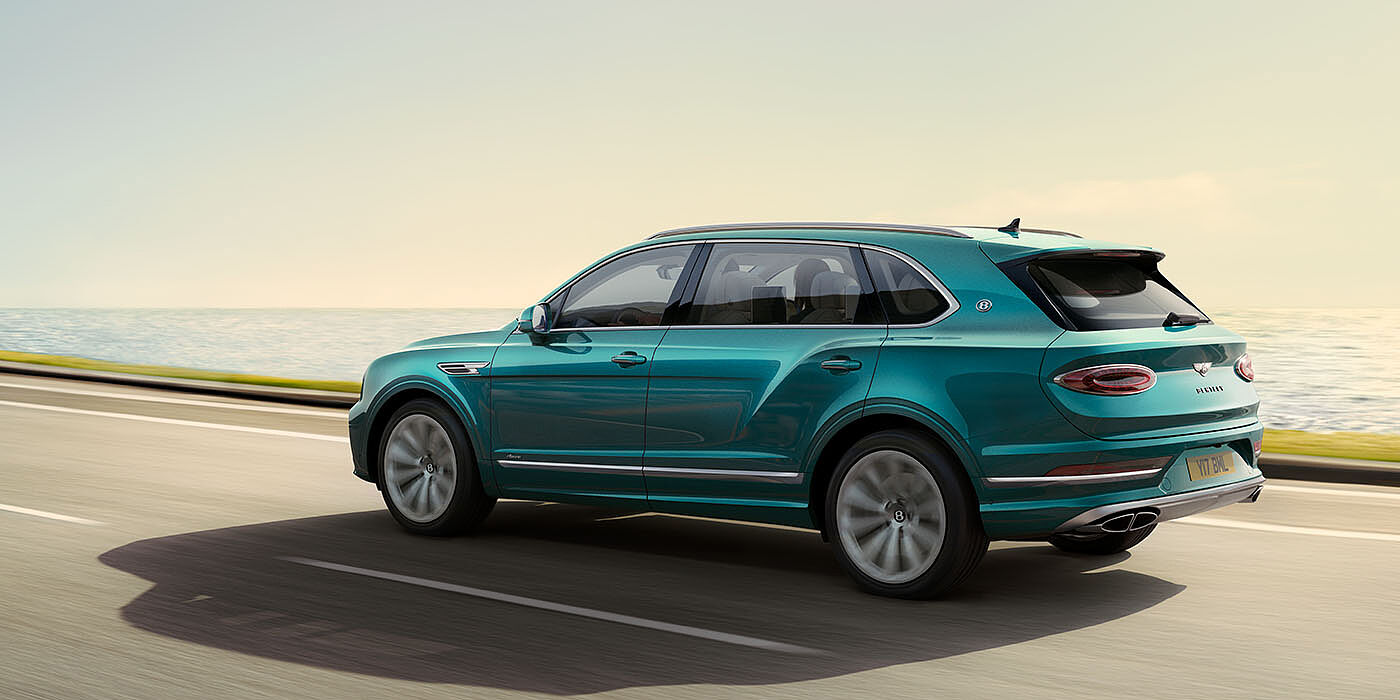 Bentley Monterrey Bentley Bentayga Extended Wheelbase Azure luxury SUV rear three quarter in Topaz Blue by Mulliner paint, driving on an ocean road.