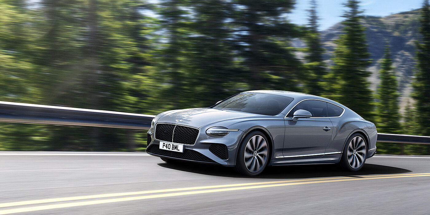 Bentley Monterrey New Bentley Continental GT coupe in Silverlake paint and 22 inch ten-spoke wheels, driving dynamically on a tree-lined road in the sunshine