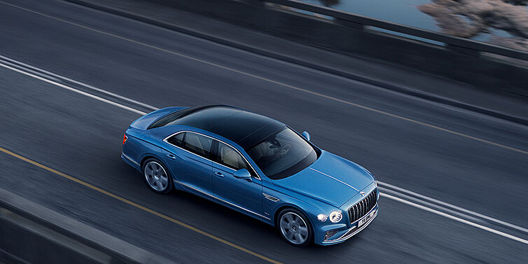 Bentley Monterrey New Bentley Flying Spur Azure sedan in Light windsor blue paint by Mulliner, with 22 inch Azure wheels seen from overhead driving dynamically on a country road