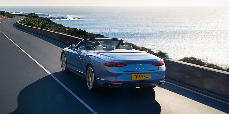 Bentley Monterrey New Bentley Continental GTC Azure convertible rear view in Light Windsor blue paint with 22 inch ten spoke wheels driving dynamically on an ocean road in the sunshine