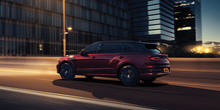 Bentley Monterrey Bentley Bentayga Extended Wheelbase Mulliner SUV in Cricket Ball red paint driving dynamically in city at night